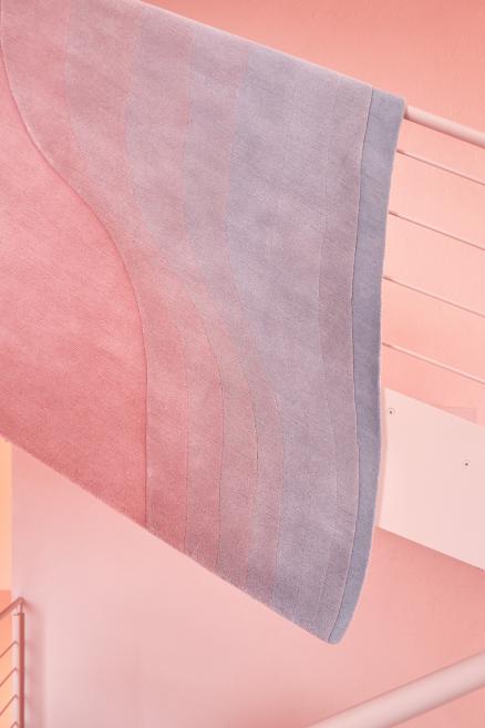 Paklājs ar rozā, zilu un pelēku dizainu. 