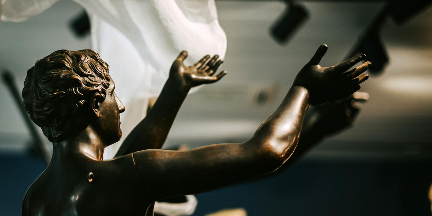 Skulptūra ar divām paceltām rokām. 