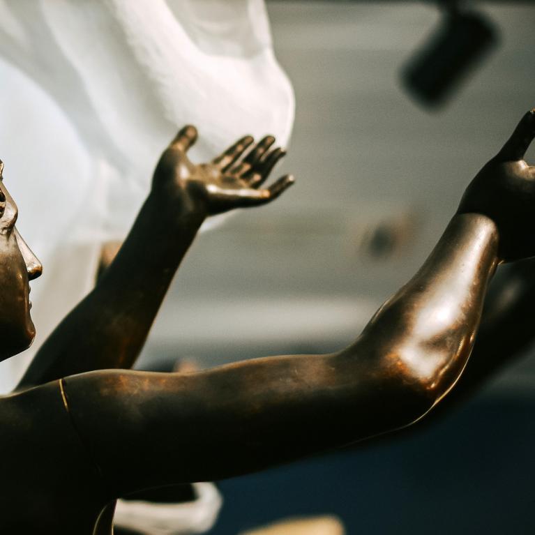 Skulptūra ar divām paceltām rokām. 