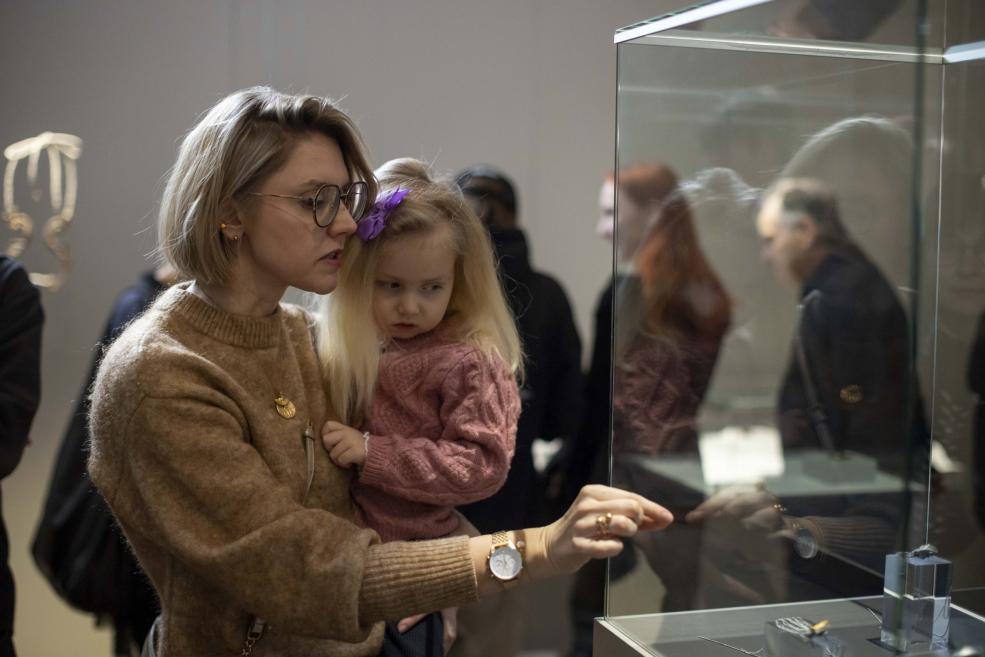 A woman with a little girl in her arms examines jewelry in a display case