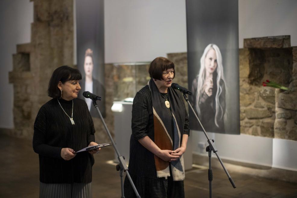 Two women speak into microphones at a jewelry exhibition